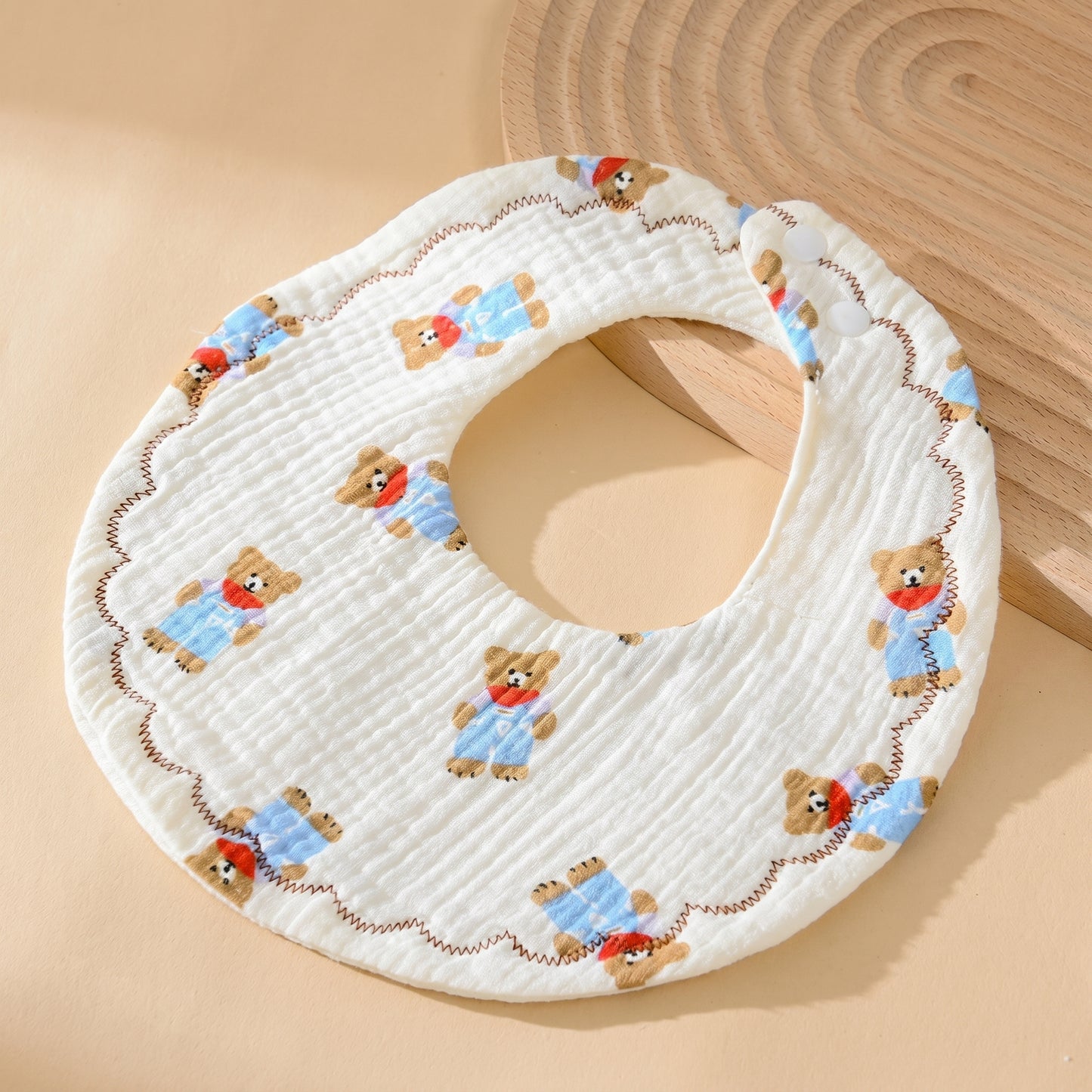 WhisperSoft™ cotton bib featuring a bear pattern, white background, and scalloped edge on a wooden surface.