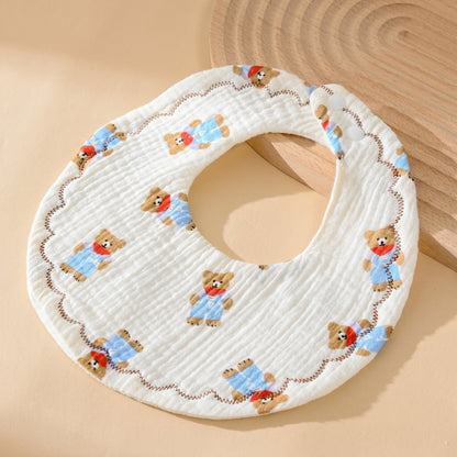 WhisperSoft™ cotton bib featuring a bear pattern, white background, and scalloped edge on a wooden surface.
