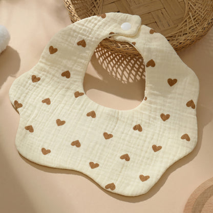 WhisperSoft™ cotton bib in light yellow with brown heart patterns, displayed on a beige surface with a woven basket.