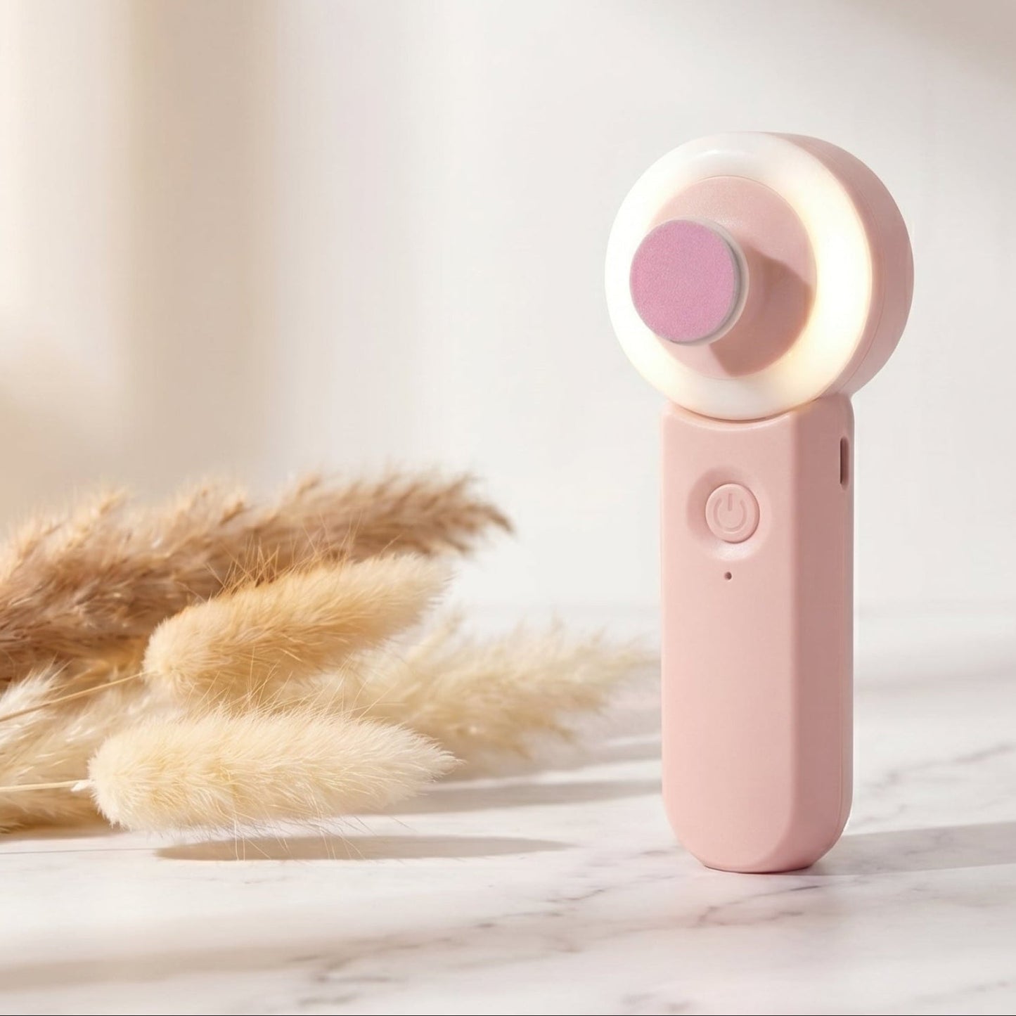 Pink handheld device with a light on a marble surface with dried plants
